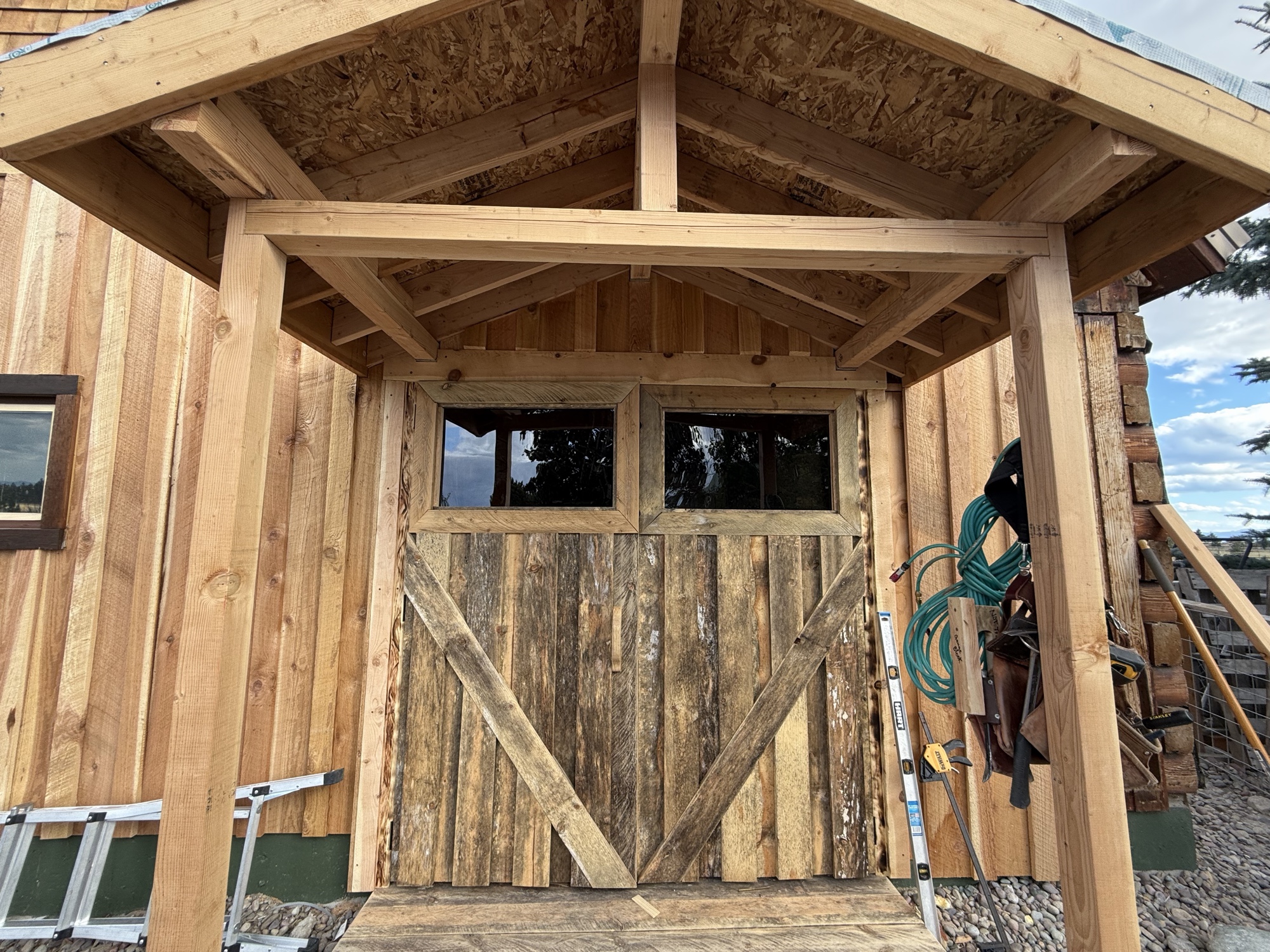 Custom reclaimed wood barn doors with glass transoms installed under a new timber porch frame
