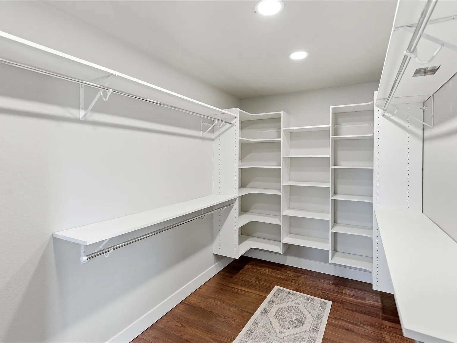 Custom walk-in closet with white built-in shelving systems and hardwood flooring