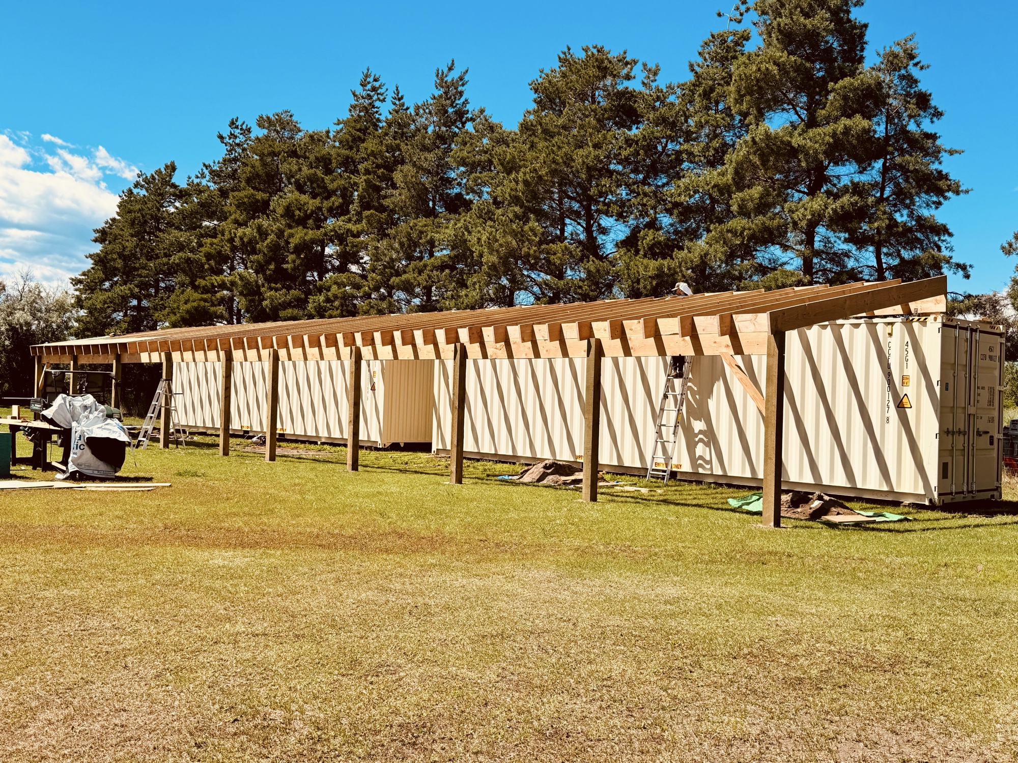 Wide view of completed container structure with full timber roof spanning multiple containers