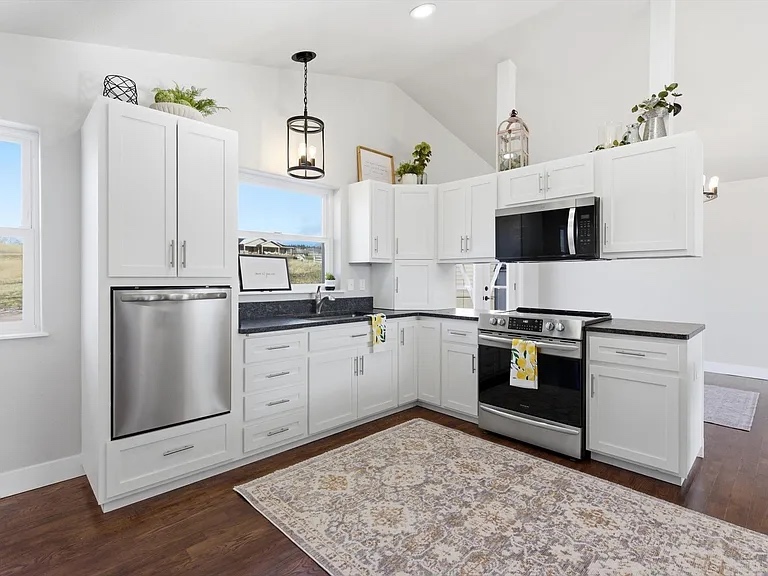 White shaker kitchen with dark granite countertops, stainless appliances, and pendant lighting